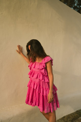 Woman in a pink dress standing against a beige wall.
