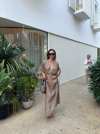 Woman in a patterned dress walking outdoors near plants and a building.